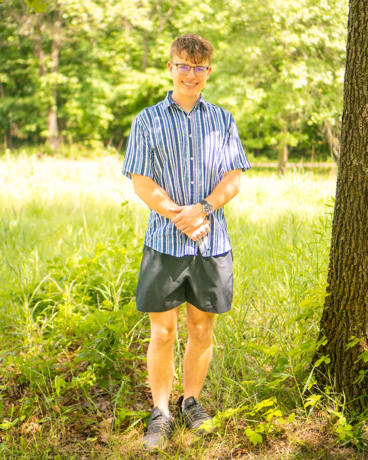 Senior portrait, candid pose by a tree in a sunlit meadow
